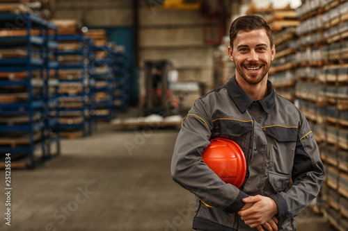 Photographie Shot of a handsome young bearded factory worker in uniform holding protective ha