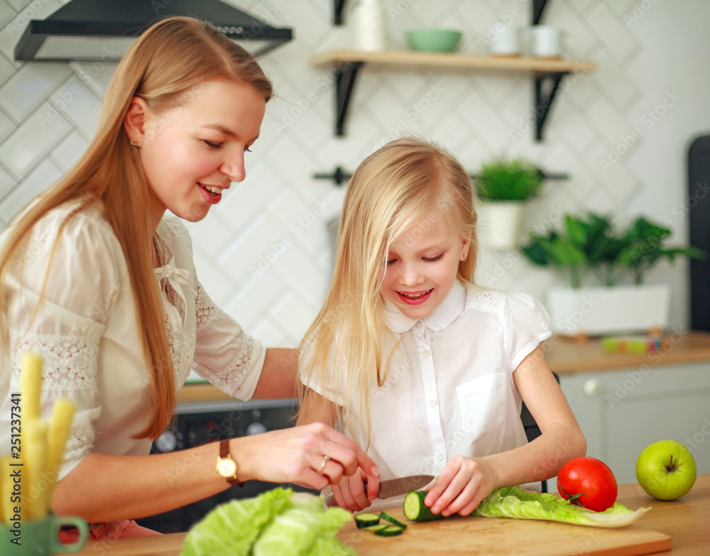 Mother with her daughter in kitchen preparing healthy food with fresh vegetables