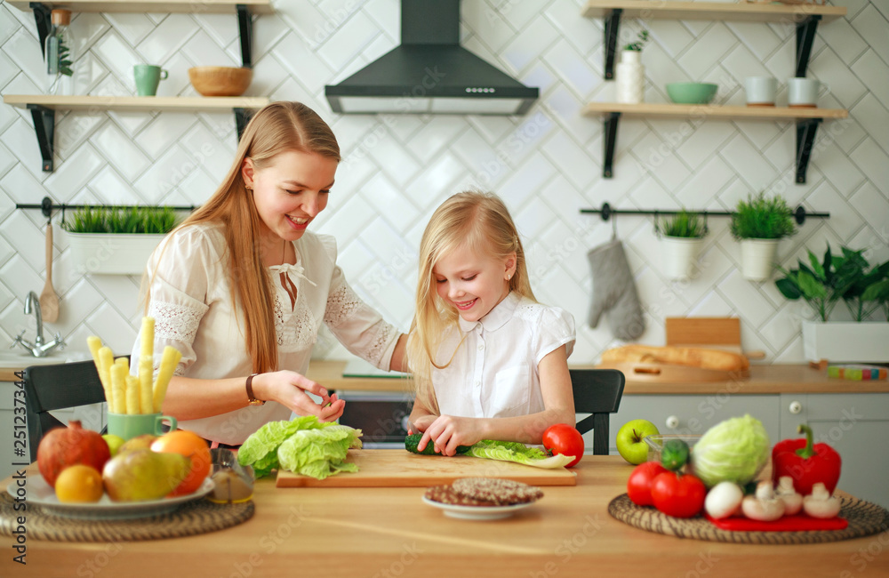 Mother with her daughter in kitchen preparing healthy food with fresh vegetables