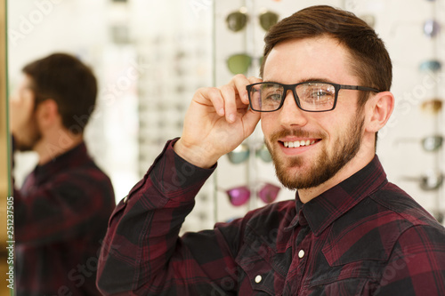 Portrait of a happy handsome man smiling to the camera wearing glasses at optics store. Attractive young man looking excited, wearing new eyeglasses. Ophthalmology, eyesight, healthcare