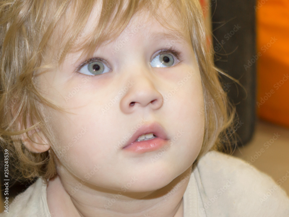 Portrait of a little boy with big blue eyes and curly blond hair. Baby looks with passion and interest up and to the side. Portrait of a little boy with big blue eyes and curly blond hair. Baby looks with passion and interest up and to the side.