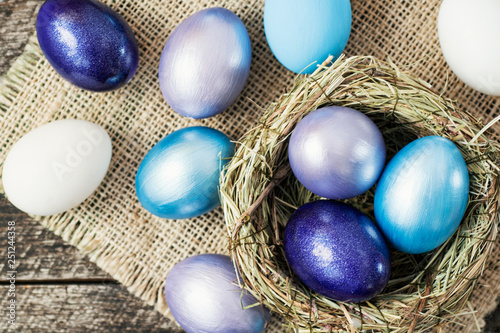 Bright purple colored Easter eggs in nest on wooden background, selective focus image. Happy Easter card