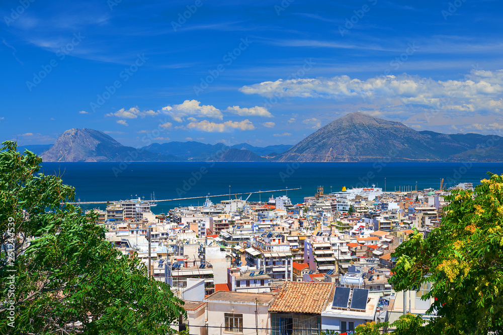 Summer panoramic view on Greece Patras city white houses and roofs, ships in harbour, Ionian sea and green mountains with blue sky and clouds in the background. Classical Greek city architecture