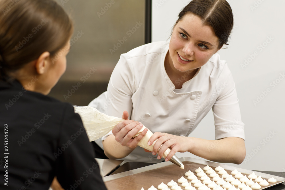 Process of discussion between two female confectioners about cooking desserts. Women preparing exclusive food with help of special tools such as confectionery bag and baking sheet. Process of discussion between two female confectioners about cooking desserts. Women preparing exclusive food with help of special tools such as confectionery bag and baking sheet.