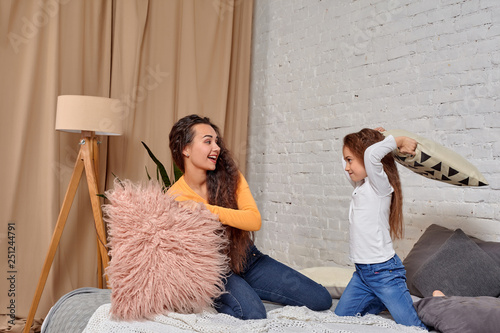 Young mom and daughter fooling around with pillow fights on the bed