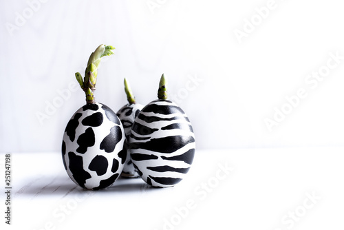 Set of easter eggs painted like zebra, cow, snow leopard on a white wooden background. From eggs bloom green leaves.
