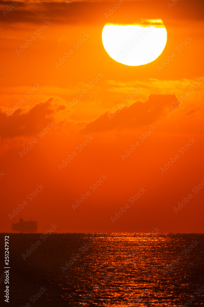 Obraz premium 波を照らす朝の太陽と渡る船