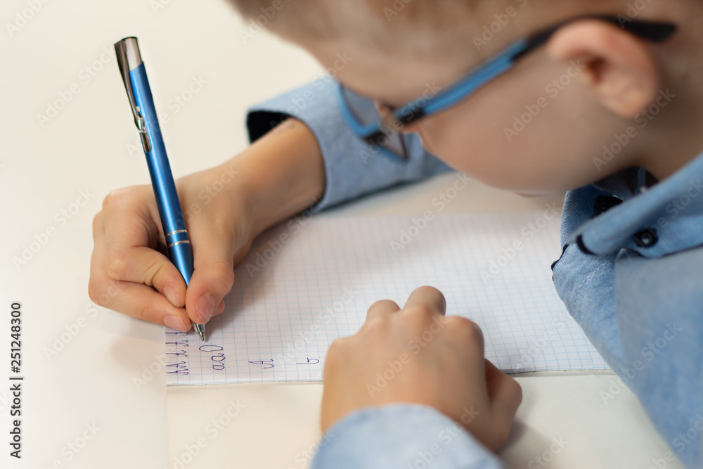 Dłonie chłopca trenującego naukę pisania. Pisanie liter długopisem w zeszycie w kratkę.  - obrazy, fototapety, plakaty 