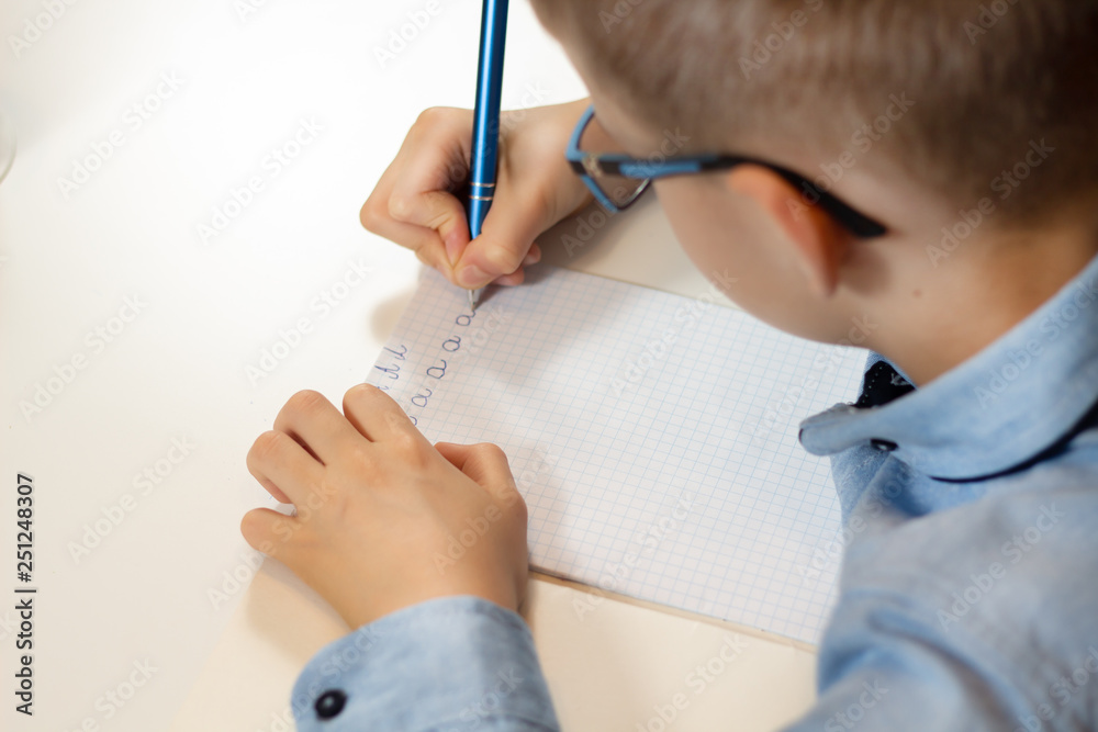 Dłonie chłopca trenującego naukę pisania. Pisanie liter długopisem w zeszycie w kratkę.  - obrazy, fototapety, plakaty 