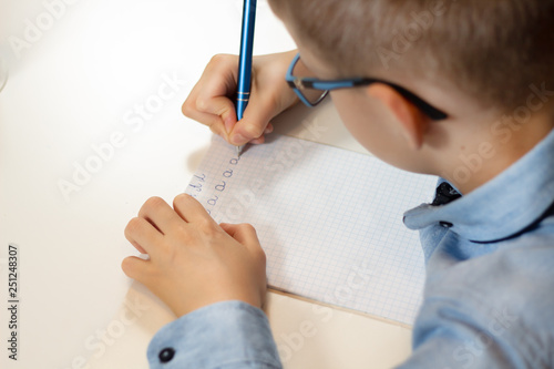 Dłonie chłopca trenującego naukę pisania. Pisanie liter długopisem w zeszycie w kratkę. 
