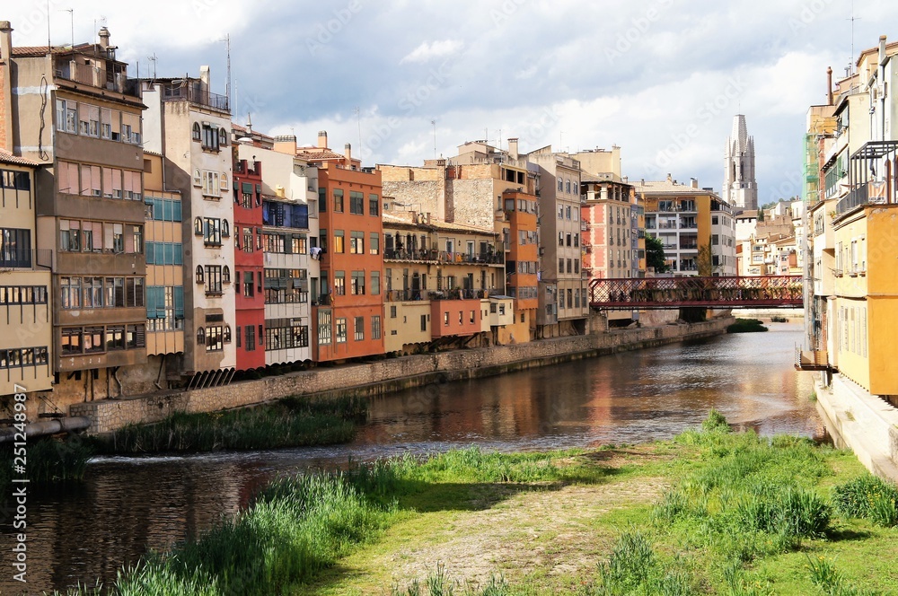 Colorful yellow, orange and red houses line the banks of the Onyar River in Girona, Catalonia, Spain with a bridge in the background