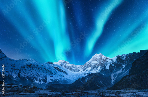 Aurora borealis above the snow covered mountain range in europe. Northern lights in winter. Night landscape with green polar lights and snowy mountains. Starry sky with aurora over the rocks. Space