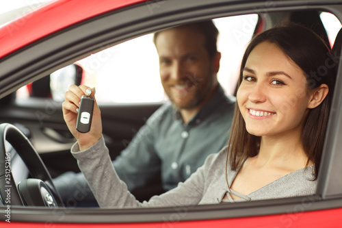 Side view of beautiful woman and bearded man sitting in car and holding keys of woman's new red car. Male manager of car dealership making deal with pretty female customer.