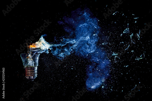 Сosmic explosion of burning light bulb with flying splinters of broken glass and smoke on isolate black background. Сoncept of creative art of starry sky, cosmos,  universe and the big bang theory.