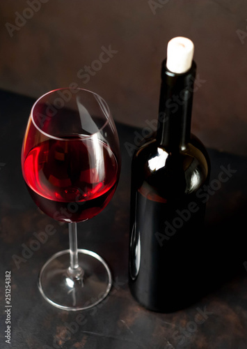 Wine glass with red wine and bottle against a stone background.