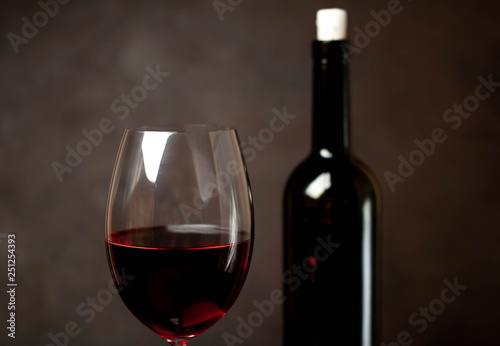 Wine glass with red wine and bottle against a stone background.