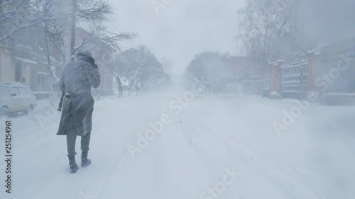 Lonely man in coat and hat walks at the street during snow storm 