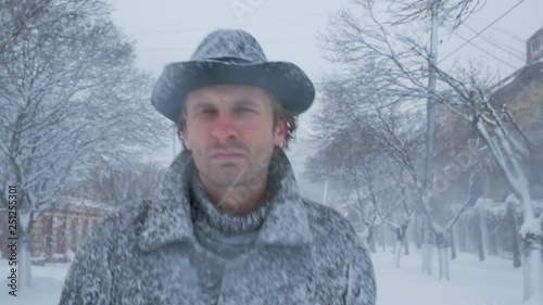 Serious man with coat and hat walks on the winter street at snowfall time close-up