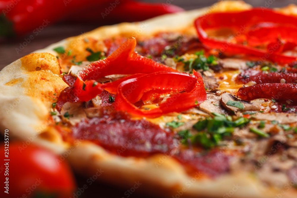 Close up Italian pizza with melted cheese, sausage, ham, salami, mushrooms, pepper and fresh herbs on a brown table decorated by mushrooms, red sweet pepper and cherry tomatoes Close up Italian pizza with melted cheese, sausage, ham, salami, mushrooms, pepper and fresh herbs on a brown table decorated by mushrooms, red sweet pepper and cherry tomatoes