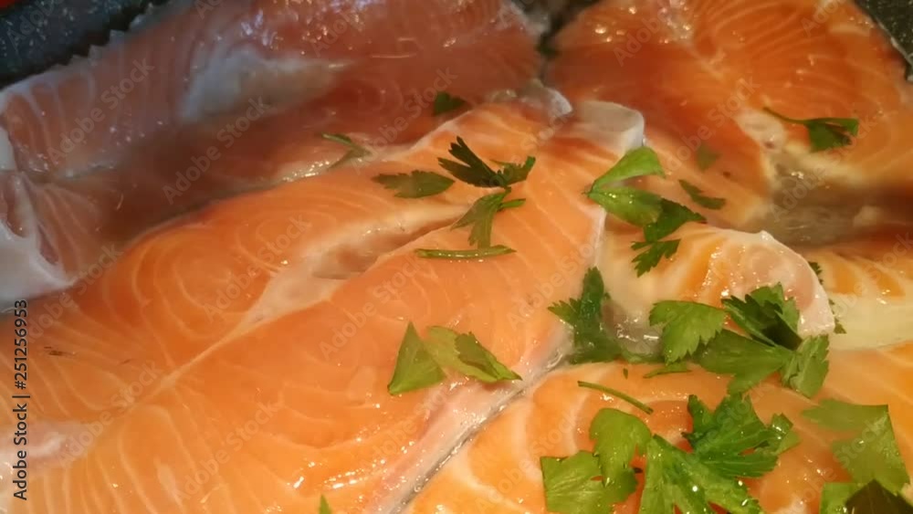 Close up on slices of salmon being cooked. The shadow of a pair of scissors in action is distinguished: crumble parsley leaves fall on the salmon. Video at 30fps 4k. Close up on slices of salmon being cooked. The shadow of a pair of scissors in action is distinguished: crumble parsley leaves fall on the salmon. Video at 30fps 4k.