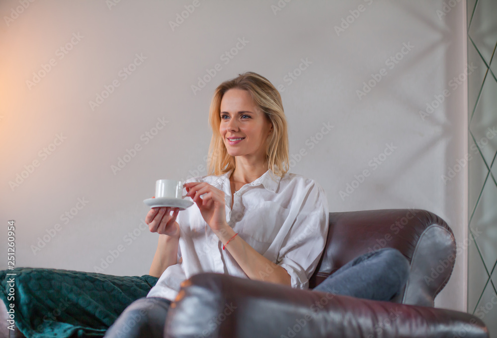 Blonde woman sitting in the armchair with coffee