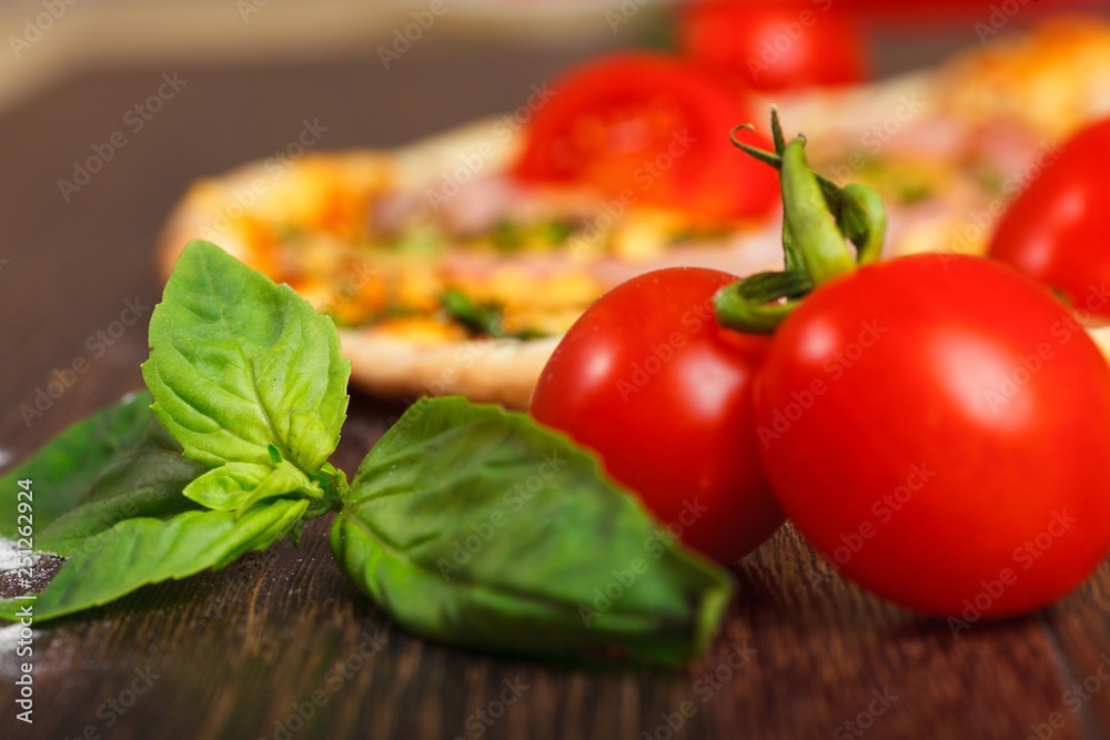 Close up top view Italian pizza with melted mozzarella cheese, red cherry tomatoes, ham and fresh green herbs on a brown table decorated by mushrooms, red sweet pepper and cherry tomatoes Close up top view Italian pizza with melted mozzarella cheese, red cherry tomatoes, ham and fresh green herbs on a brown table decorated by mushrooms, red sweet pepper and cherry tomatoes