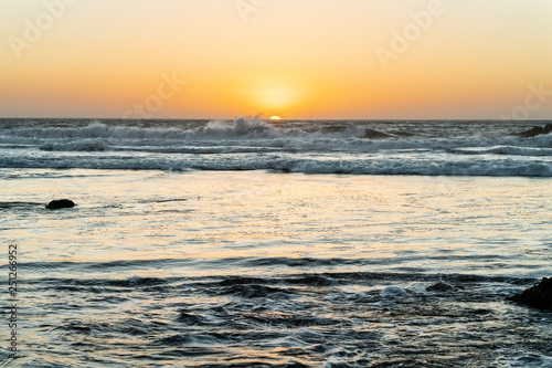 Sun goes down below a water horizon in the middle of the Pacific Ocean making a wonderful and colorful landscape with twilight at a Chilean wild beach. Nice shadows and reflections with orange tones