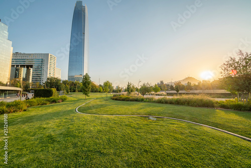 Sunset at a green park in Santiago de Chile city. A colorful modern city skyline, with the sun going down behind Cerro San Cristobal Hill. An awe cityscape with light and shadows