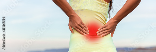 Fitness sport woman touching lower back in pain banner panorama header crop. Closeup of hands pressing on red area showing painful muscles.