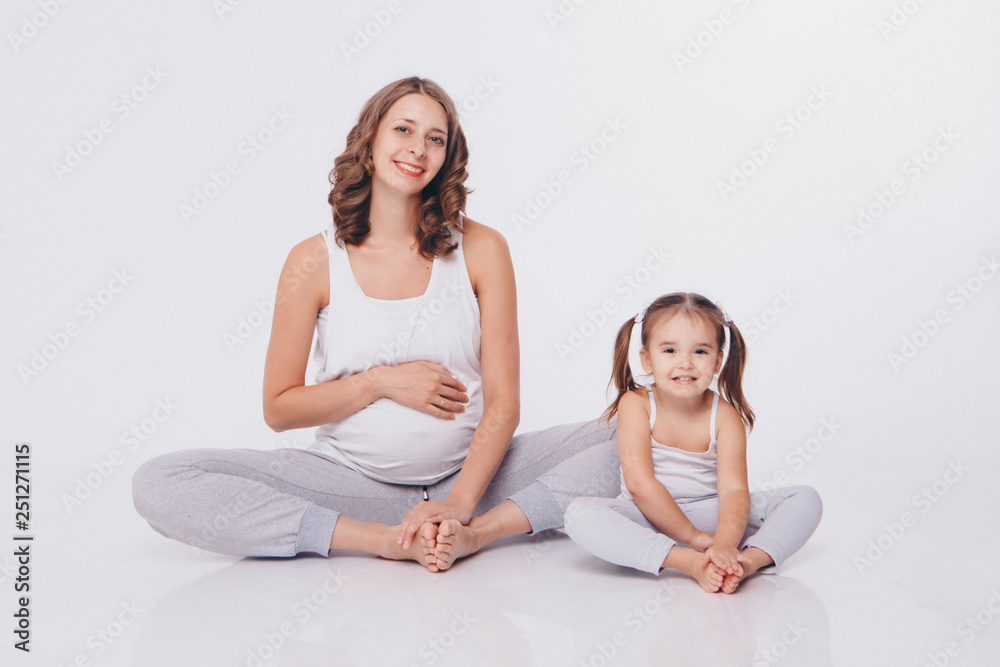 international women day: pregnant woman and little girl in tracksuits sitting on the floor on white background international women day: pregnant woman and little girl in tracksuits sitting on the floor on white background