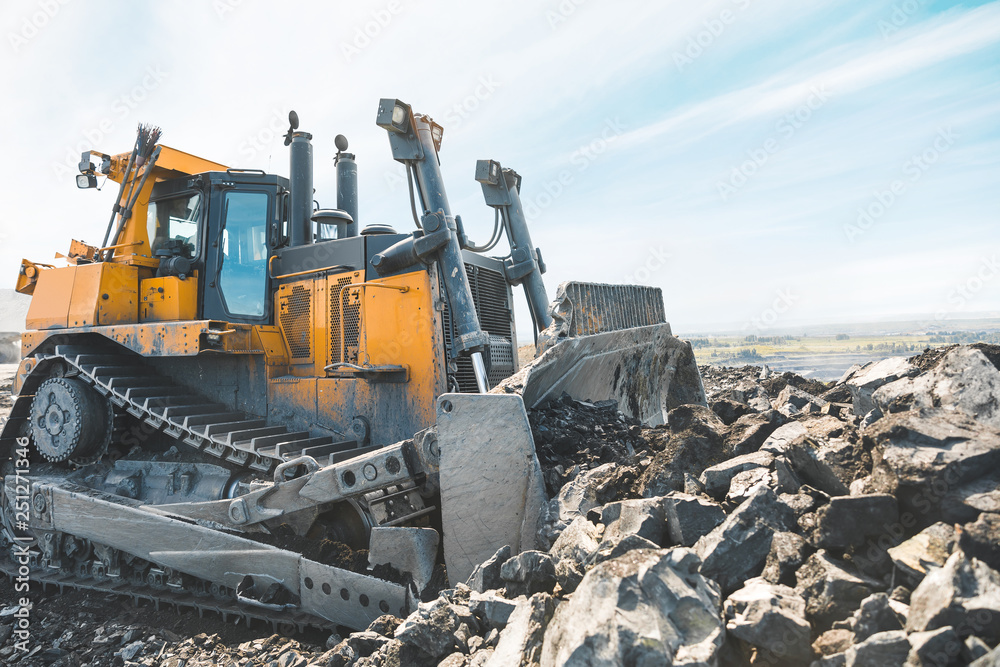Yellow excavator in career moves overburden. Bulldozer combs the ground, with the bright sun and nice blue sky in the background Yellow excavator in career moves overburden. Bulldozer combs the ground, with the bright sun and nice blue sky in the background