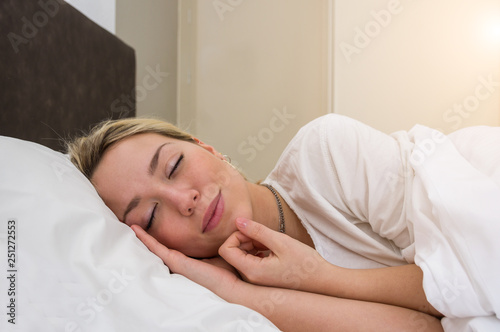 Portrait of a peaceful blonde woman sleeping on a white bed in the morning photo