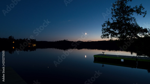 Tranquil peaceful late sunset - early evening on Hungry Jack Lake with dock / pier, moon, stars, and cabins off the Gunflint Trail in Northern Minnesota 