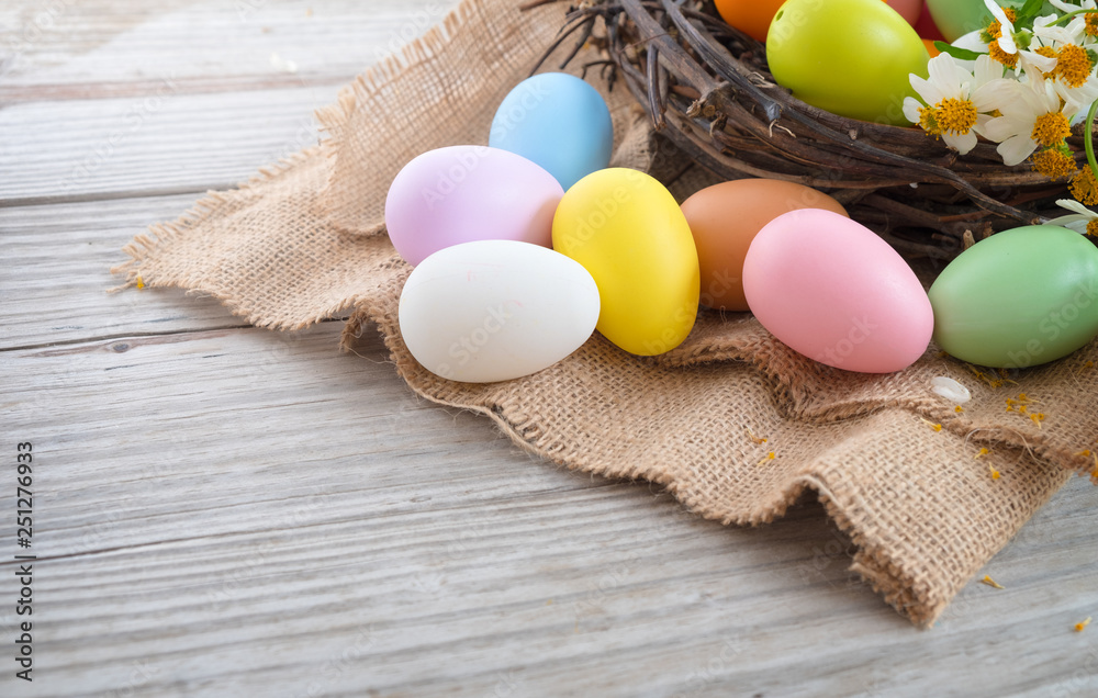 Colorful Easter eggs in nest with flower on rustic wooden planks background. Holiday in spring season. vintage pastel color tone. Close up composition.