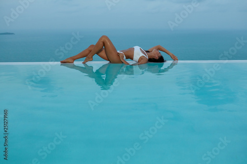 Summer. Woman model in fashion swimsuit on edge of swimming pool.