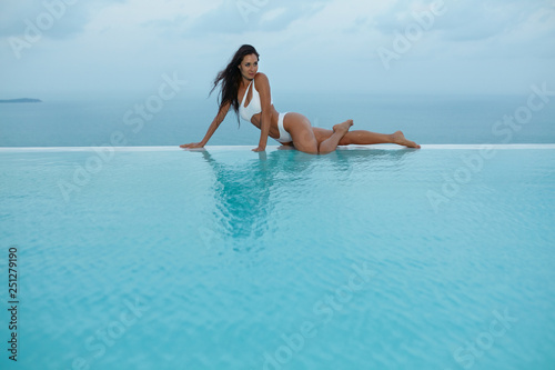 Summer. Woman model in fashion swimsuit on edge of swimming pool.