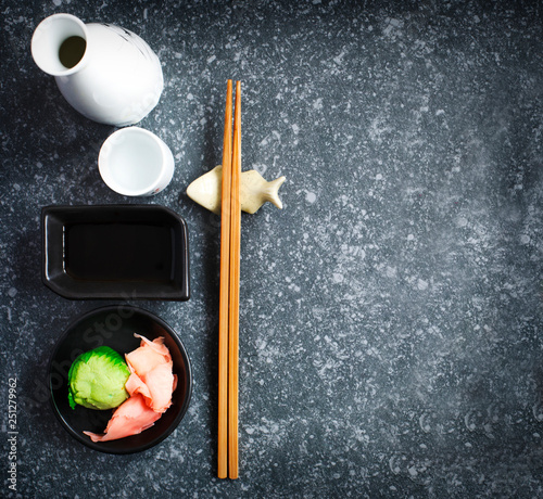 Asian food background with copy space. Sake, chopsticks, wasabi and ginger on dark grey concrete background, flat lay