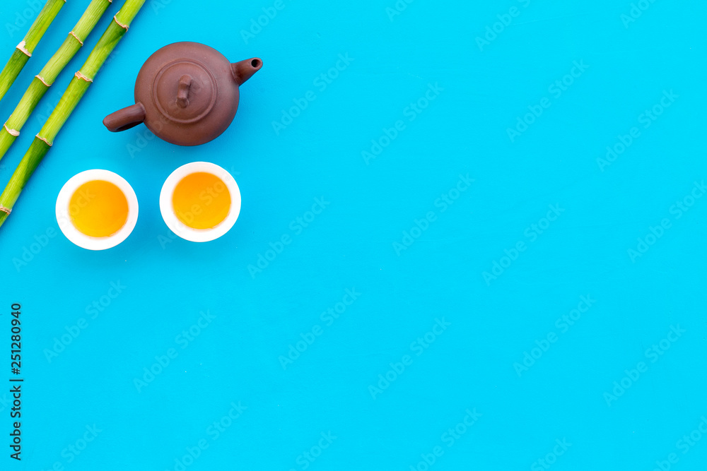 Asian tea traditions. Drink tea. Tea ceremony. Tea pot near cups of green tea and bamboo decoration on blue background top view copy space Asian tea traditions. Drink tea. Tea ceremony. Tea pot near cups of green tea and bamboo decoration on blue background top view copy space