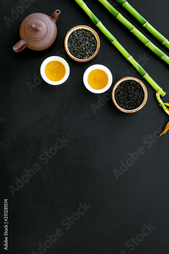 Chinese tea ceremony concept. Tea pot, tea cup, dry tea leaves on black background top view copy space
