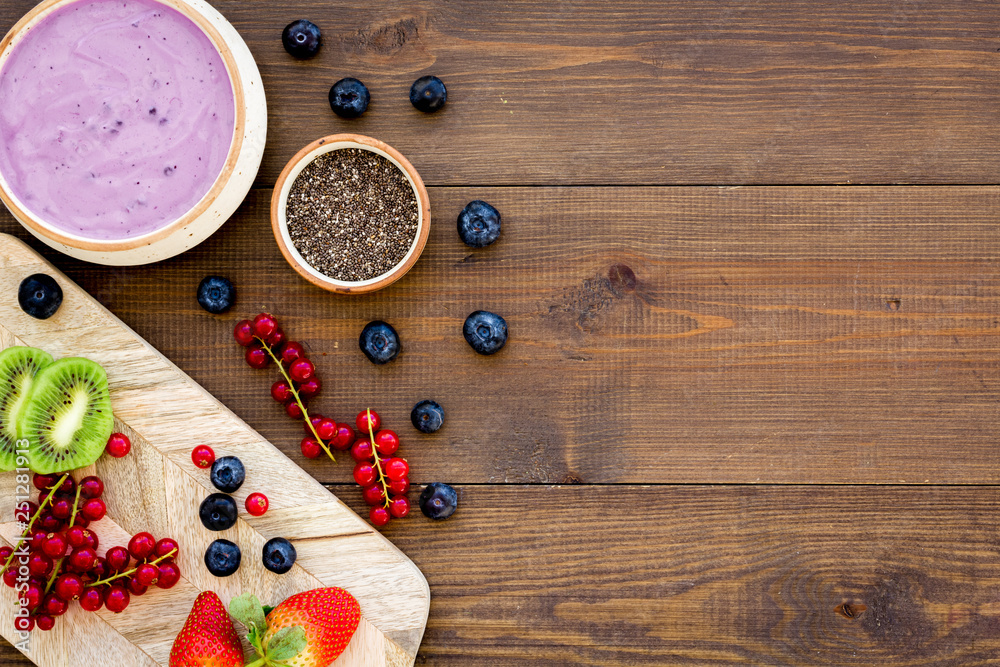 Cook trendy breakfast. Acai smoothie bowl near cutting board with fresh fruits, berries, chia seeds on dark wooden background top view copy space Cook trendy breakfast. Acai smoothie bowl near cutting board with fresh fruits, berries, chia seeds on dark wooden background top view copy space