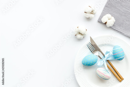 Easter table decoration in blue colors. Plate, cutlery, painted eggs and dry cotton flowers, tablecloth on white background top view space for text