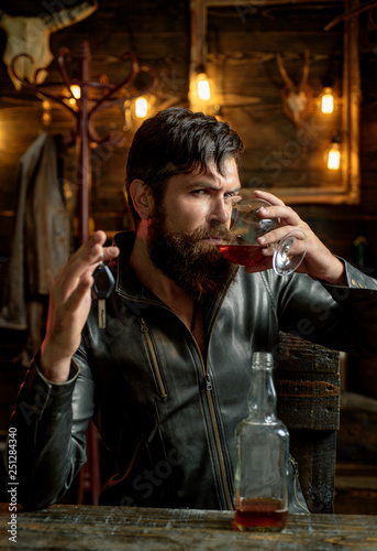 Man with beard holds glass brandy. Macho drinking. Degustation, tasting. Handsome stylish bearded man. Confident man with car keys in his hand.