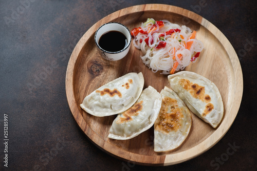 Round wooden serving tray with pan fried korean potstickers, studio shot on a dark brown metal background
