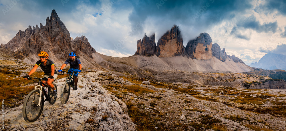 Fototapeta premium Cycling woman and man riding on bikes in Dolomites mountains andscape. Couple cycling MTB enduro trail track. Outdoor sport activity.