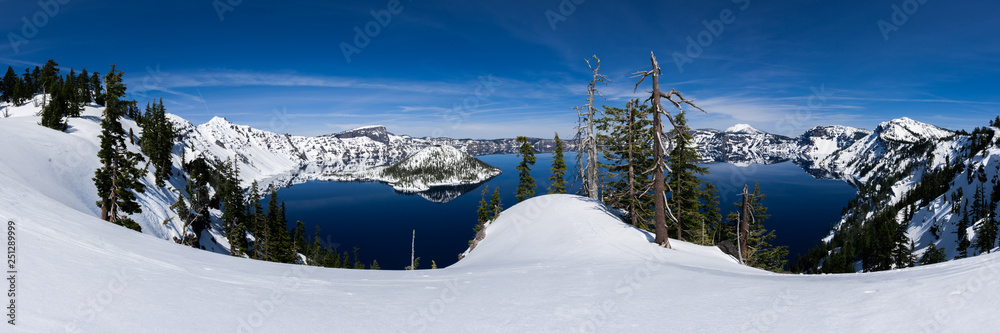 Panoramic of Crater Lake with snow on a sunny day.
