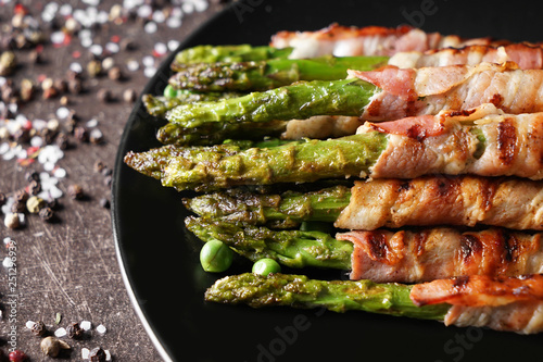 Plate with bacon wrapped asparagus on grey table, closeup