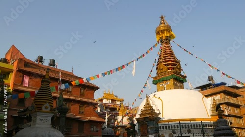 Colorful prayer flags wawing in the wind over Stupa temple, Holy Pagoda, symbol of Nepal and Kathmandu with Buddha's Eyes. Sunset ligth. tibetan buddhism. Pigeons flying over ancient architecture.