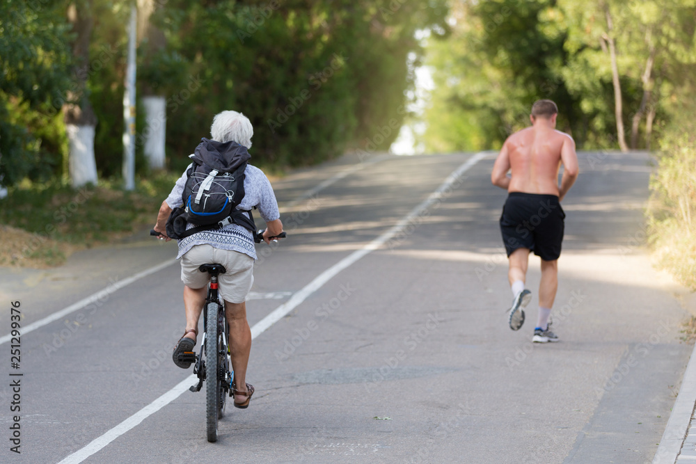 Obraz premium elderly woman riding a bicycle, young man with a naked torso running, playing sports outdoors