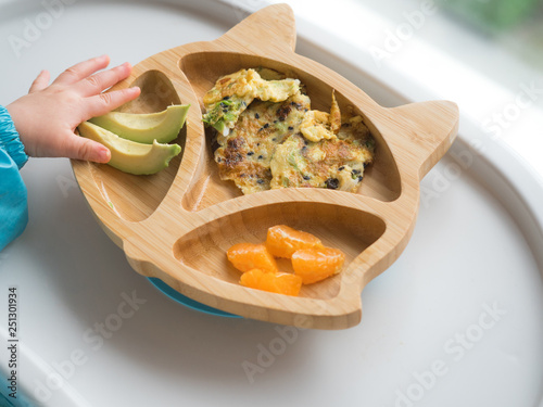 Baby eating by hands, Baby eating organic bio vegetables with BLW method, baby led weaning. Happy vegetarian kid. Toddler eat himself, self-feeding. infant baby eating. Omelette with orange, avocado