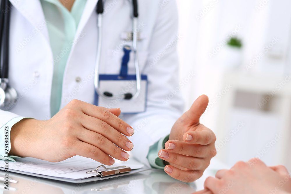 Unknown doctor and patient talking while sitting at the desk in hospital office, close-up of human hands. Medicine and health care concept Unknown doctor and patient talking while sitting at the desk in hospital office, close-up of human hands. Medicine and health care concept